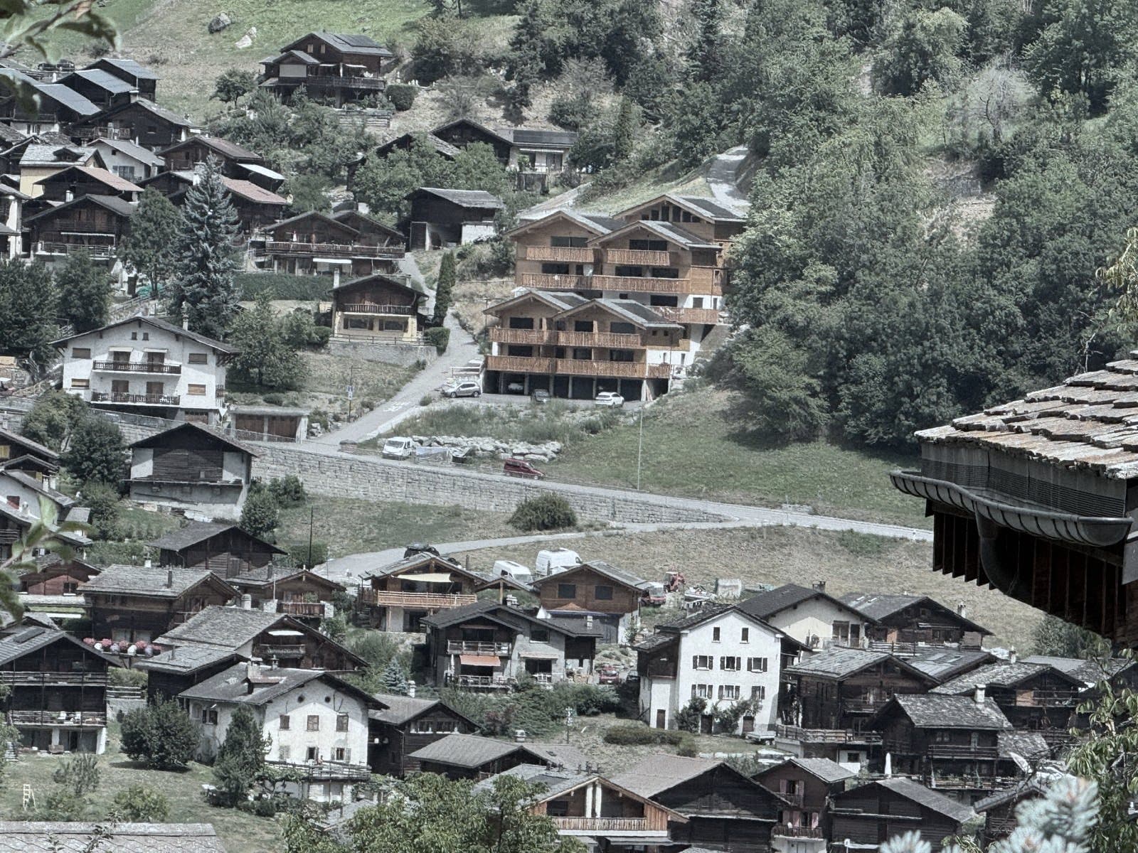 Le versant du village au téléobjectif : mazots anciens, maisons blanches et immeubles récents en bois se partagent la pente.
