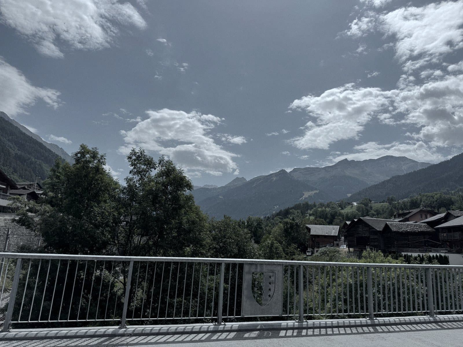 Depuis le pont sur la Dranse : un écusson découpé dans le garde-corps, les mazots et le fond de la vallée.
